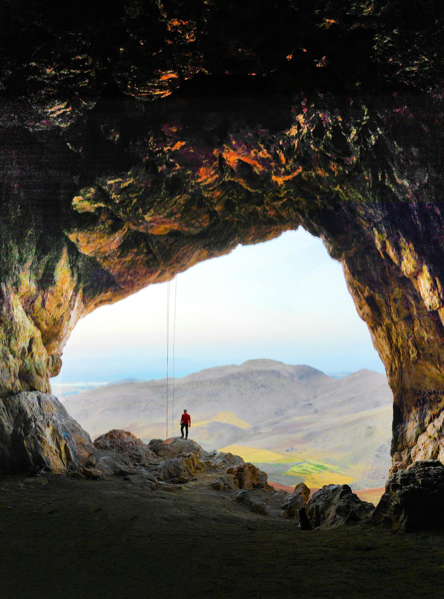 A lone explorer stands at the entrance of a vast cave in Maragheh, Iran.