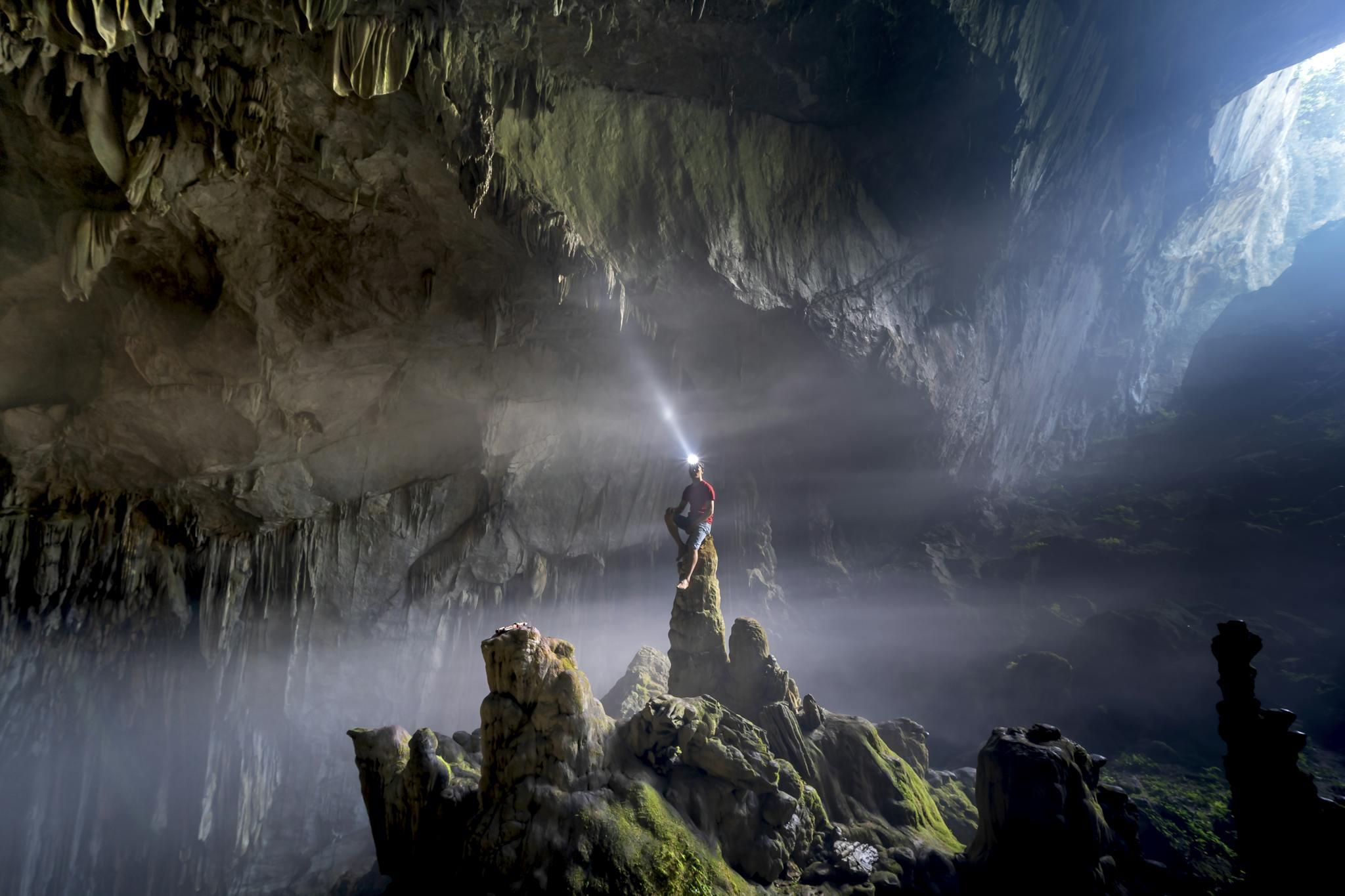 Adventurer with a headlamp illuminating a vast, rocky cave interior.